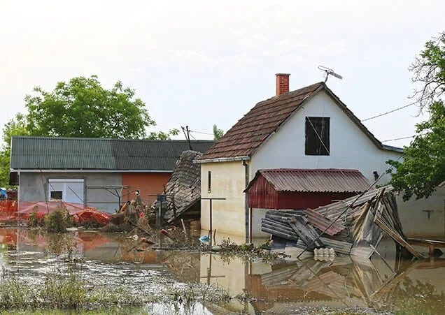 A flooded residential street with partially submerged houses and vehicles. 