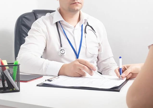 The doctor is pointing at the document while the patient holds a pen, appearing to sign or fill out a form.