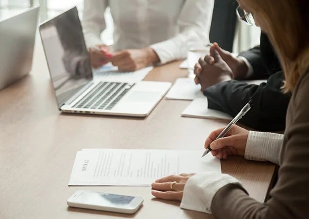 A close-up of a professional meeting where three people are seated at a wooden table.