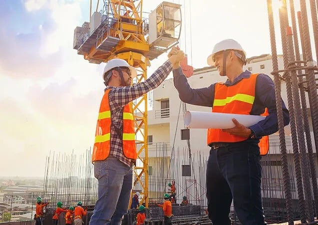 protect-contractors-and-subcontr A construction worker wearing a safety vest and helmet stands at a job site, reviewing documents.